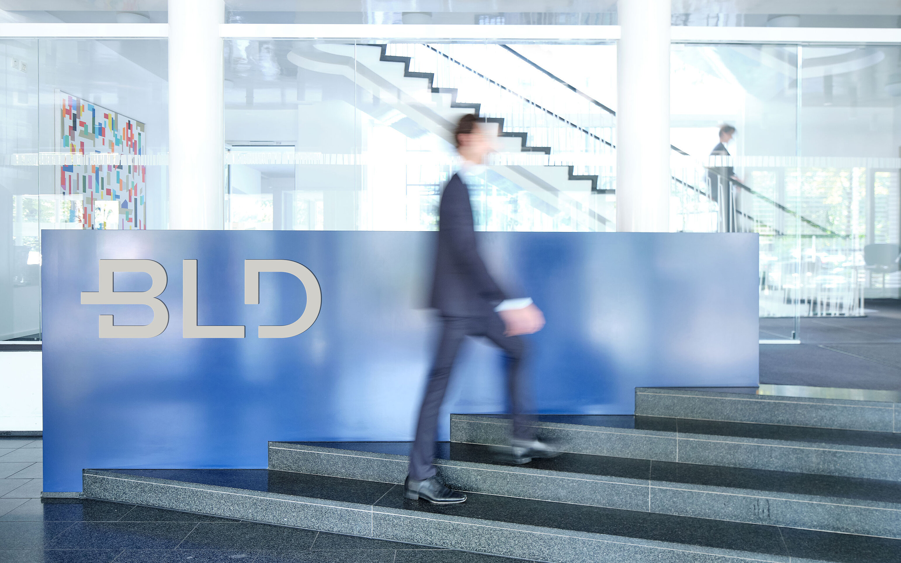 Das ist ein Imagebild von BLD. Es ist der Eingangsbereich des Kölner Standorts zu sehen. Auf dem Bild geht eine Person in einem Anzug die Treppe hoch.